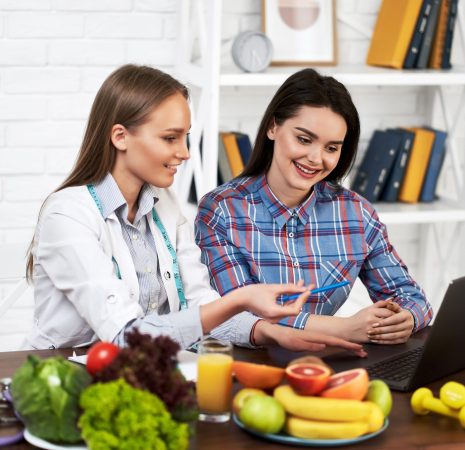 A smiling nutritionist advises a young patient woman on proper nutrition and dieting. The doctor shows in laptop a scheme of weight loss without a bad effect on health. 
Diet based on vegetables and fruits for girls.